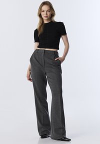 Černý zkrácený top s krátkými rukávy, kombinovaný s šedými širokými kalhotami s vysokým pasem. Hladká tkanina s sklady a postranními kapsami. Černé boty.