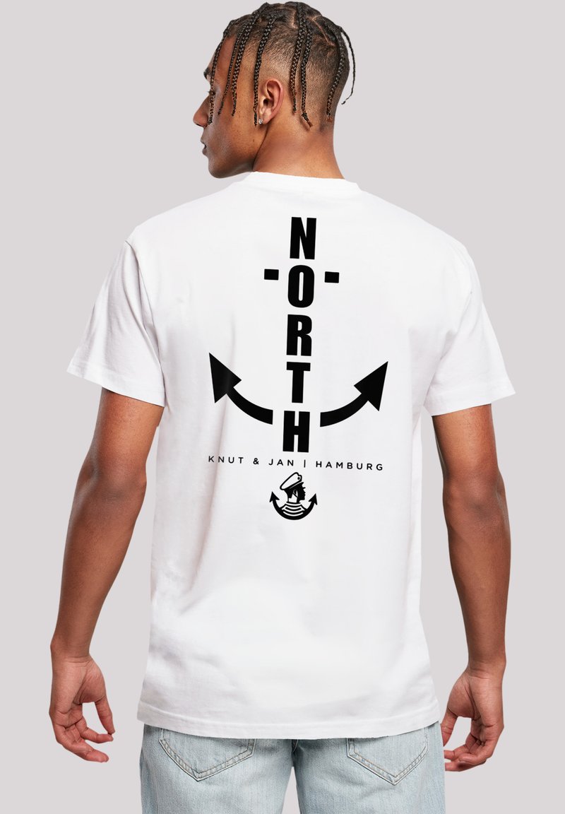 White cotton t-shirt featuring bold black text "NORTH" vertically aligned, arrows graphic, and "Knut & Jan | Hamburg" text below.