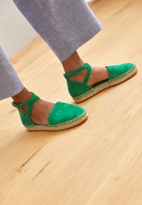 Gröna mocka espadrillos med rund tå, ankelrem och vävd jutesula. Ytan har en slät textur med kontrasterande sömnadsdetaljer.