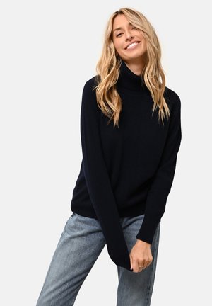 Maglione a collo alto blu navy realizzato in morbido tessuto a maglia, con una vestibilità comoda e polsini a coste, abbinato a jeans azzurri.