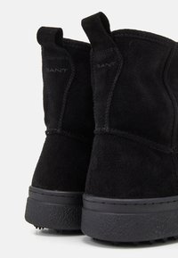 Schwarze Wildleder-Stiefeletten mit einer strukturierten Oberfläche und Gummisohlen, die eine glatte Oberfläche und minimalistische Designelemente aufweisen.