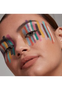 Närbild av ett ansikte med livfull, randig smink i blått, rosa, gult och grönt; mjuka läppar i en matt persikoton; slät hudstruktur.