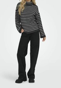 Schwarz-grauer gestreifter Rollkragenpullover mit lockerer Passform und weitem Ärmeln, kombiniert mit hochgeschnittenen schwarzen Jeans und klobigen schwarzen Schuhen.