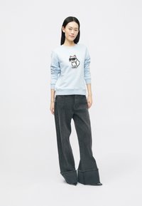 Sweatshirt azul claro com um gráfico de gato em cartoon, combinado com jeans pretos largos com punhos largos e detalhe de costura central.