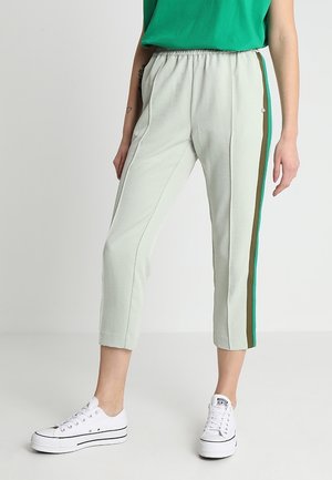 Person iført lysegrå korte bukser med grønne og brune sidelommer og hvide sneakers med lavt snit.