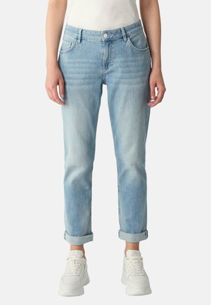 Light blue cuffed jeans worn with white chunky sneakers, shown from waist to feet on a person wearing a white top.