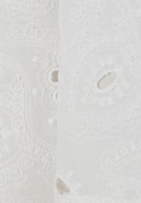 Tessuto bianco con ricami intricati caratterizzati da motivi circolari e piccoli intagli, che mostrano una superficie texturizzata e dettagli delicati.