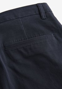 Detailný záber na tmavomodré nohavice s vreckom typu welt vzadu a pútkom na opasok na páse.