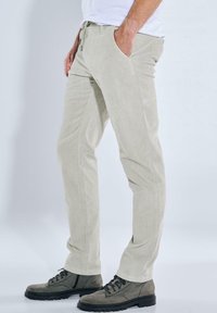 Helle beige Cordhosen mit schmalem Schnitt, zwei Seitentaschen und einem Kordelzugbund, kombiniert mit dunkelgrauen Schnürstiefeln.