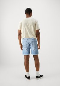 Camicetta corta beige chiaro con maniche corte, pantaloni shorts in denim blu chiaro con risvolti, sneakers nere e calzini bianchi. Design semplice, vestibilità casual.