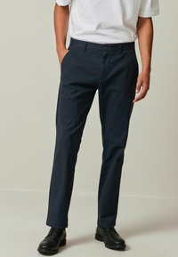 Pantaloni navy blue dintr-un material ușor, cu croială dreaptă, având două buzunare laterale, închidere cu un singur buton și o textură subtilă.