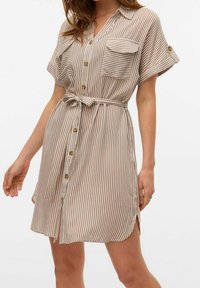 Abito a camicia a righe in beige e marrone chiaro con chiusura a bottoni frontale, maniche corte, due tasche sul petto e una cintura annodata in vita.