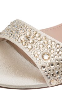 Μπεζ σανδάλι με σατινέ φινίρισμα, με φαρδιά επάνω επιφάνεια διακοσμημένη με καθαρά και χρυσά στρας, και λεία σόλα.