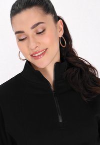Maglione zip-up nero con colletto alto. Tessuto morbido, trama liscia. Presenta una cerniera frontale e dettagli di cucitura discreti.
