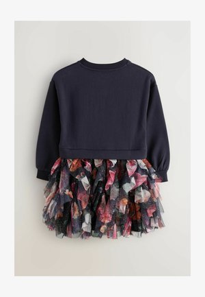 Tumši zils džemperis ar garām piedurknēm, kombinēts ar spilgtu, slāņotu tilla svārku, kas rotāts ar ziedu motīviem un mirdzošām detaļām.