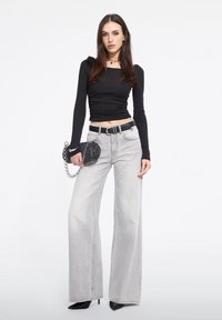 Top negro de manga larga con escote cuadrado, combinado con unos vaqueros de denim de pierna ancha y cintura alta en color gris claro. Sosteniendo un bolso negro con detalles de cadena.