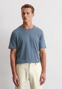 Himmelblaues kurzärmeliges T-Shirt aus weichem, strukturiertem Stoff mit Rundhalsausschnitt, getragen zu beigen Leinenhosen.