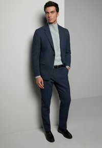 Marineblå skræddersyet jakkesæt med en struktureret lysegrå sweater, suppleret med et sort bælte og blanke sorte sko. Glat finish og struktureret pasform.