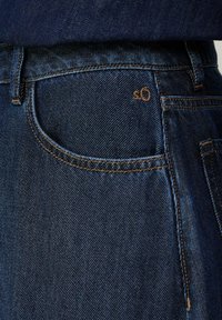 Jeans in denim blu scuro con tasca frontale, cuciture arancioni a contrasto e un piccolo etichetta conlogo sulla vita.