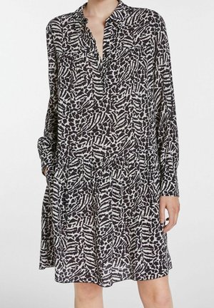 Robe à motifs noir et blanc avec manches longues, col à boutons, et deux poches poitrine. Coupe évasée avec taille froncée. Tissu léger.