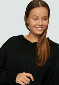 Sweat à capuche noir en tissu tricoté texturé, avec une coupe décontractée et une poche avant discrète. Manches longues et design minimal.