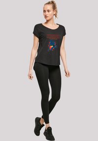 Black t-shirt with short sleeves featuring "Stranger Things" graphic in color. Paired with black leggings and black athletic shoes.