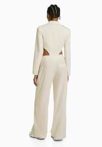 Beige tailored suit with cut-out back, long sleeves, and wide-leg pants. Features structured shoulders and minimalistic design.