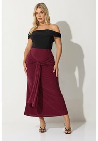 Off-the-shoulder svart topp med en figurnära vinröd kjol som har en vriden detalj framtill och flödande tyg. Svarta remsandaler fulländar looken.