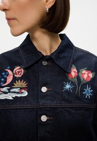 Σκούρο τζιν μπουφάν με πολύχρωμα κέντημα λουλουδιών και ουράνιων σωμάτων, ασημένιους κουμπίες και κλασικό σχέδιο γιακά.