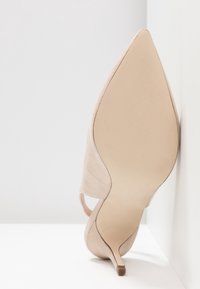 Chaussure à talon haut beige avec un bout pointu, en daim doux. Dispose d'un talon fin et d'une semelle lisse avec un détail antidérapant en caoutchouc.