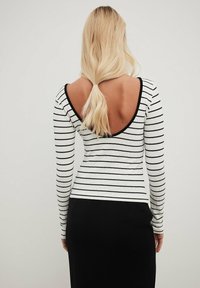 Vit långärmad topp med svarta horisontella ränder, med en djup skuren ryggdesign och ribbad textur. Kombinerad med en svart kjol.