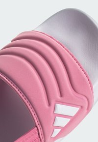 Ροζ σανδάλι slide με λεπτομερή ύφανση στην επάνω πλευρά, που διαθέτει τρεις λευκές ρίγες και καμπυλωτό σχέδιο. Λείο πέλμα με διακριτική λάμψη.