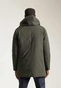 Parka verde oliva con capucha ajustada, textura suave y corte recto. Presenta costuras mínimas, ofreciendo un aspecto limpio y moderno por la parte de atrás.
