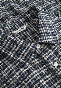 Marineblaues und cremefarbenes karierter Hemd aus strukturiertem Stoff mit Button-Down-Kragen, ausgestattet mit weißen Knöpfen und einem Markenetikett.