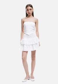 Vit strapless topp med en åtsittande bodice, kombinerad med en flerlagrad vit kjol med texturerad tyg och scalloped nederkant.