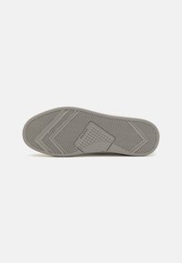Gray rubber shoe sole with herringbone pattern, textured sections, and logo detail. Flat design suited for comfort and traction.