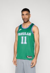 Πράσινη μπασκετική φανέλα Nike με την επιγραφή «DALLAS» σε λευκά γράμματα, τον αριθμό 11 σε μπλε, με μπλε λεπτομέρειες και υφή από δίχτυ. Ορατά γκρί σορτς.