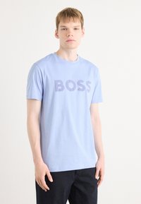 T-shirt en coton bleu clair avec le mot "BOSS" en lettres majuscules de couleur violet foncé. Encolure classique et manches courtes, texture lisse.