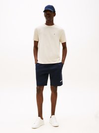 Navy shorts, light beige t-shirt with small logo, navy cap. White sneakers, relaxed fit, smooth fabric, and minimalistic design.