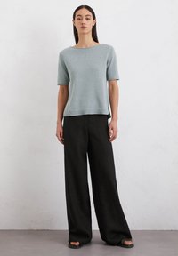 Helles blaues gestricktes Kurzarmoberteil mit weitem Ausschnitt, kombiniert mit schwarzen weit geschnittenen Hosen, vor einem neutralen Hintergrund präsentiert.
