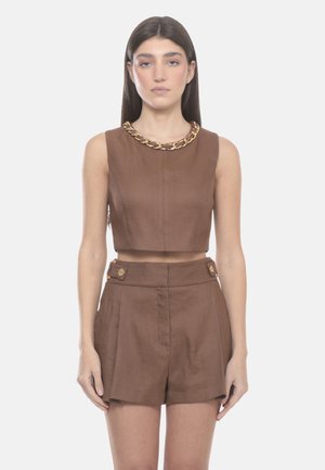 Donna con capelli lunghi e scuri che indossa un top corto marrone senza maniche con scollo con catena dorata e pantaloncini a vita alta abbinati con dettagli con bottoni.