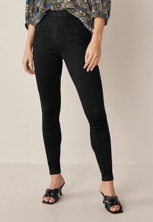 Pantalon noir slim porté avec des sandales à talons ouvertes noires et un haut à manches longues à motif floral.