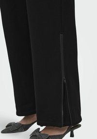 Pantaloni negri cu detaliu de fermoar lateral, confecționați dintr-un material moale; asortați cu pantofi gri cu o fundă decorativă și un design cu vârful ascuțit.