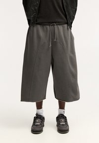 Grå överdimensionerade shorts i mjukt tyg, med elastisk midja, dragsko och svepande sömdetaljer. Bärs med svarta sneakers.