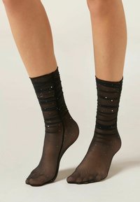 Calze nere trasparenti alla caviglia con design arricciato, decorate con punti bianchi. Presentano una finitura morbida e testurizzata e un design con punta aperta.