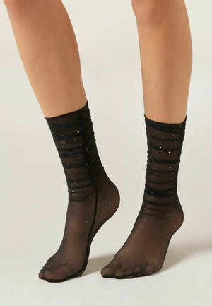 Sort gennemsigtige ankelstrømper med rynket design, prydet med hvide prikker. Har en blød, tekstureret finish og åben tå-design.