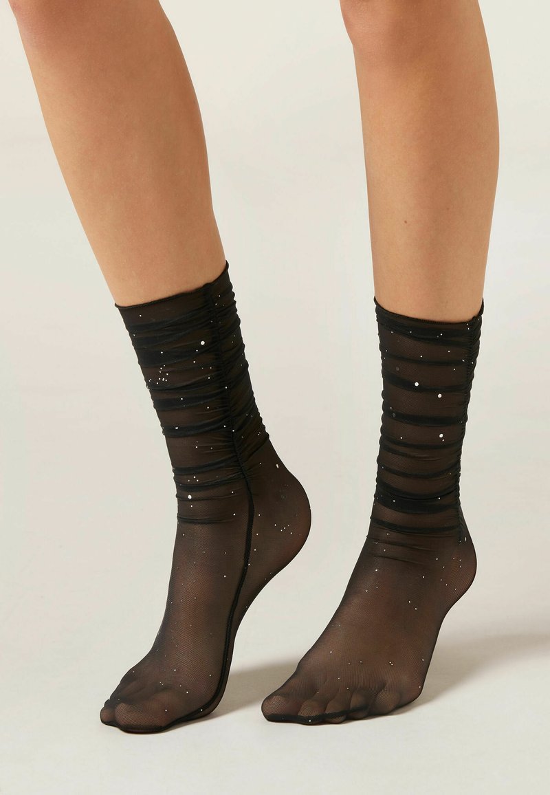 Calze nere trasparenti alla caviglia con design arricciato, decorate con punti bianchi. Presentano una finitura morbida e testurizzata e un design con punta aperta.
