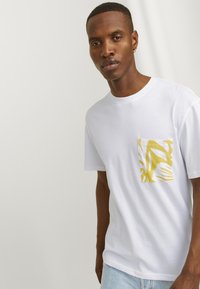 Hvid bomulds T-shirt med en gul mønstret lomme. Korte ærmer, rund hals, afslappet pasform, glat tekstur og minimalistisk design.