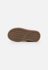Suela de zapato de goma marrón con un patrón de tracción texturizado y un borde curvado. Presenta un emblema central de logo y un indicador de tamaño.