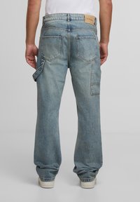 Hellblaue Denim-Cargohosen mit lockerer Passform, die mehrere Taschen, ein Lederpatch-Label und eine leicht ausgewaschene Textur aufweisen.